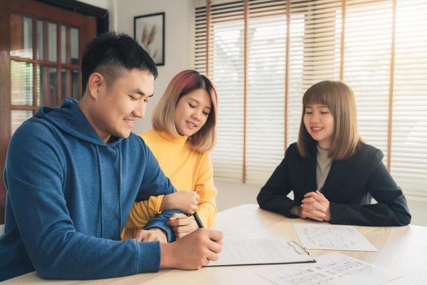 happy-young-asian-couple-and-realtor-agent-cheerful-young-man-signing-some-documents-while-sitting-at-desk-together-with-his-wife-buying-new-house-real-estate-signing-good-condition-contract-photo